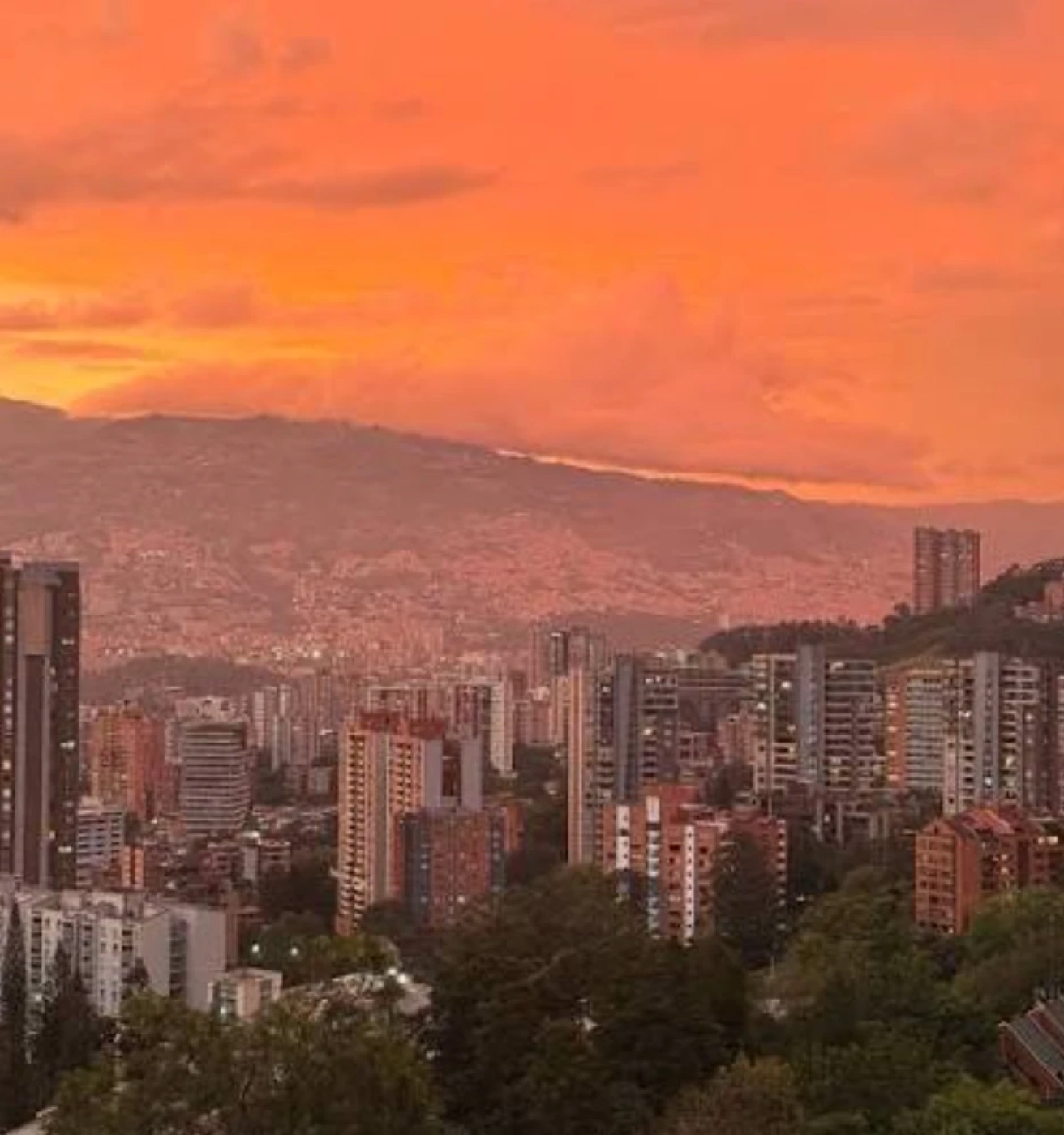 Medellín at sunset: an orange sky over the towers of El Poblado and the hills behind.