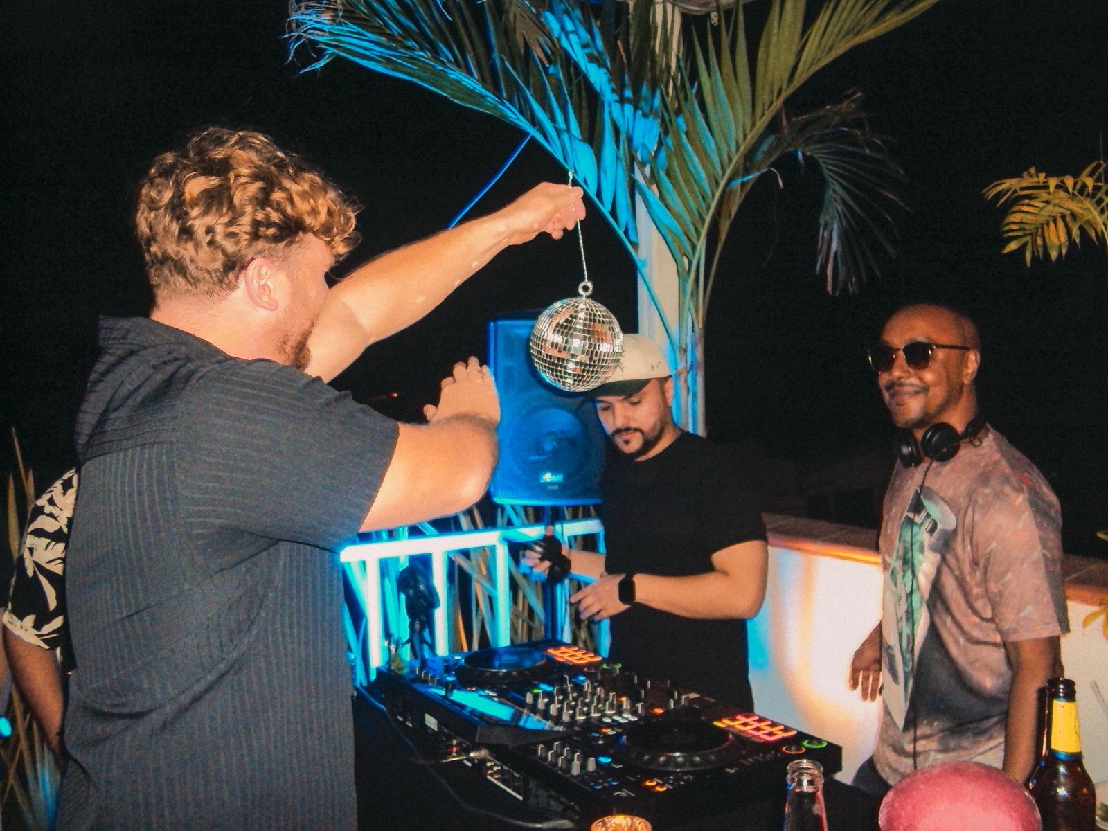 A guest holds a mini disco ball over the DJ decks on the rooftop while the DJs play.