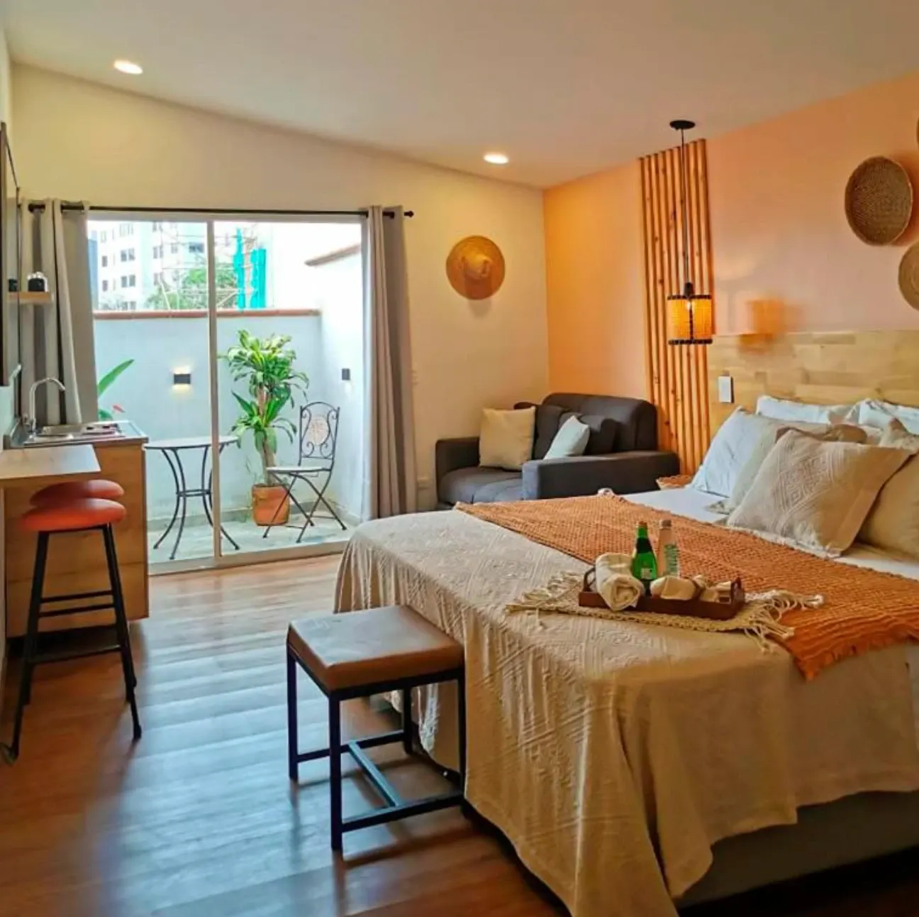 A room with a desk, bar stools, a sofa and a balcony.